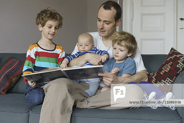 Happy family reading book while sitting on sofa at home