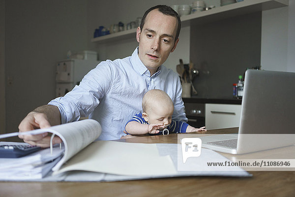 Seriöser Vater  der seinen Sohn trägt und zu Hause Dokumente liest.