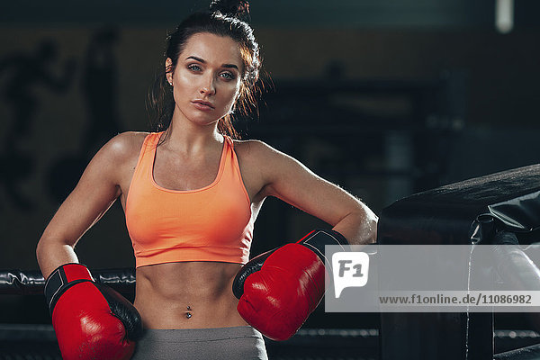 Porträt einer selbstbewussten Boxerin  die sich an einem Seil im Boxring stützt.