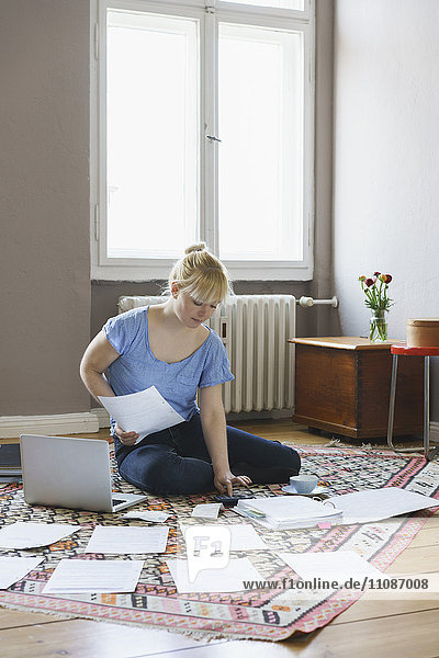 Frau macht Papierkram  während sie zu Hause auf dem Teppich sitzt.