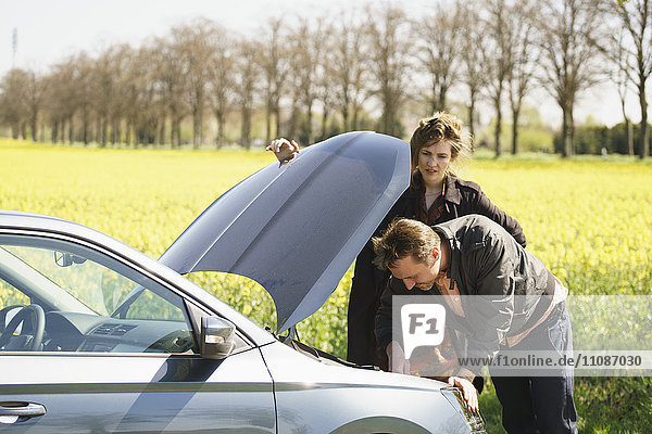 Woman looking at man repairing car by field