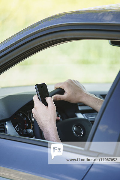 Beschnittenes Bild der Hand mit dem Smartphone im Auto