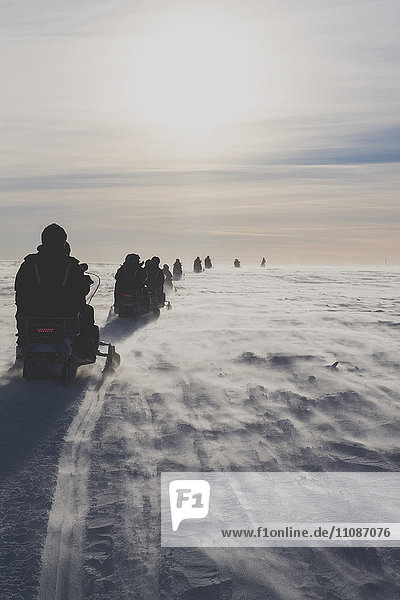 Rear view of people driving snowmobiles against sky on sunny day