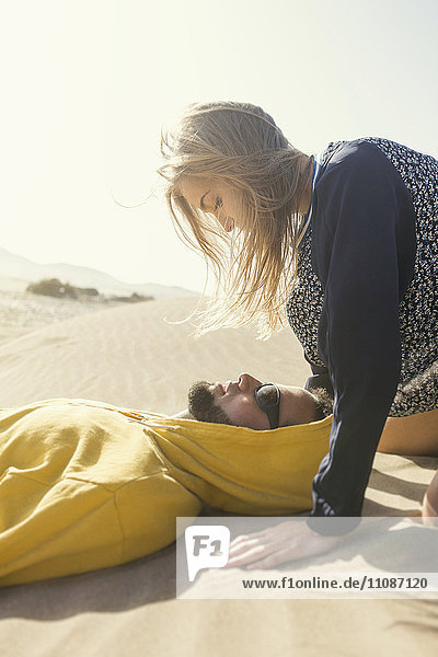 Seitenansicht der romantischen jungen Frau mit Blick auf den auf Sand liegenden Mann