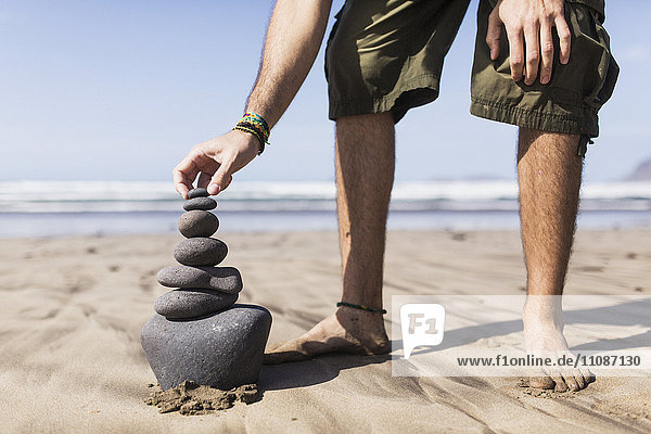 Low section of man balancing stack of stones on beach