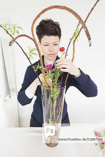 Mittlere erwachsene Frau arrangiert Blumen in Glasvase auf dem Tisch zu Hause