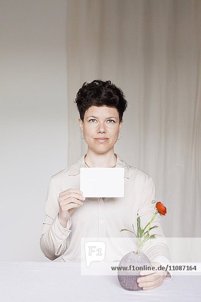 Porträt einer mittleren erwachsenen Frau mit leerer Karte und Blumenvase am Tisch