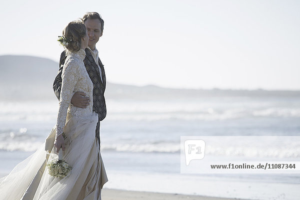 Romantische Braut und Bräutigam schauen sich am Strand an.