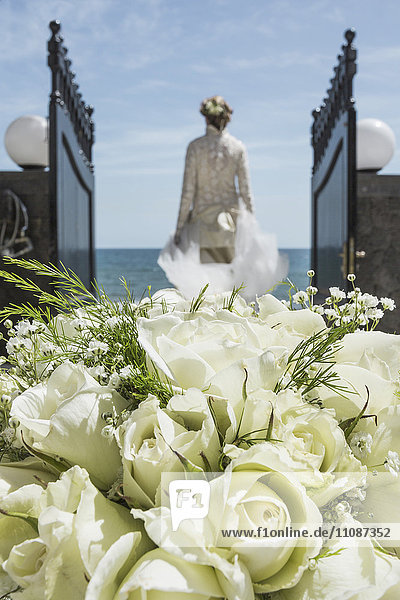 Rückansicht der Braut beim Spaziergang zum Strand mit Fokus auf Rosenstrauß im Vordergrund