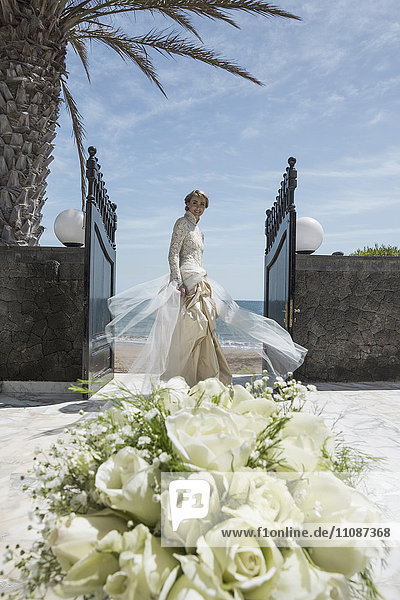 Portrait der glücklichen Braut am Eingang stehend mit Rosenstrauß im Hintergrund