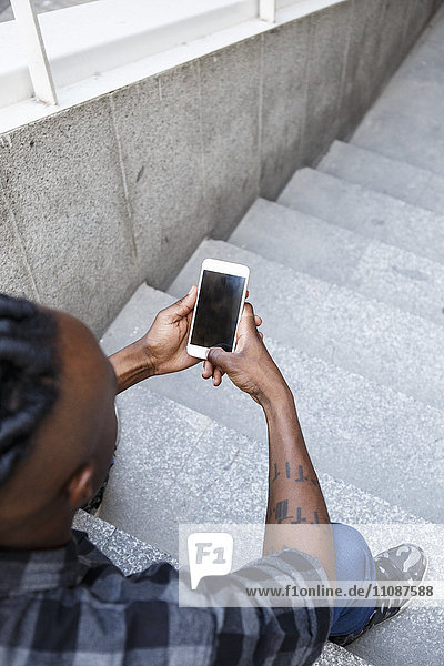 Junger Mann sitzt auf einer Treppe und benutzt ein Smartphone.