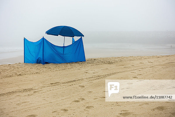 Blaues Zelt und Sonnenschirm am Strand gegen den Himmel bei nebligem Wetter