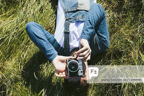 Young man lying on a meadow photographing viewer