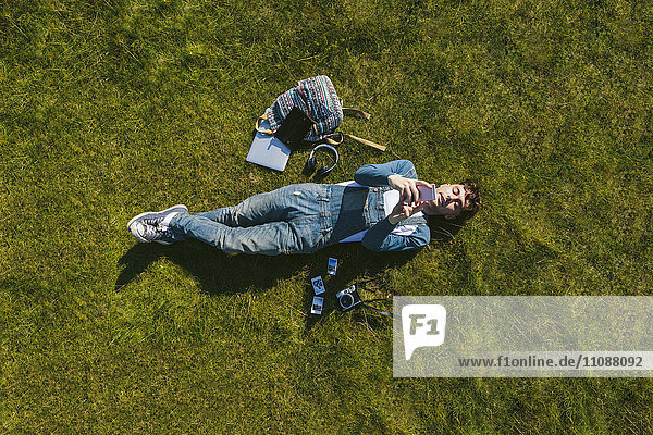 Relaxed young man lying on a meadow using cell phone  top view