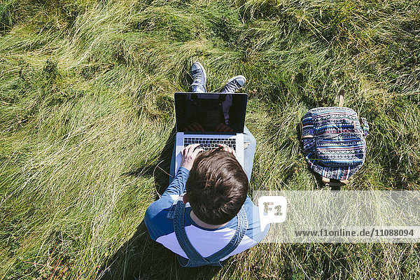 Top view of young man sitting on a meadow using laptop