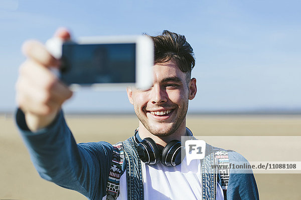 Young man taking selfie with smartphone on the beach