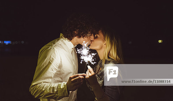 Küssendes junges Paar  das nachts am Strand Funkeln hält.
