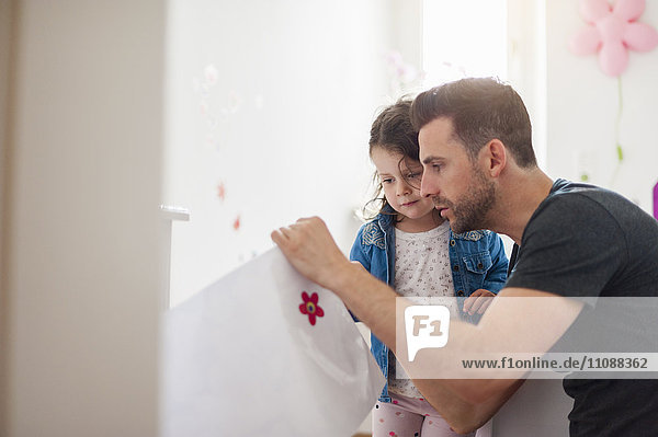 Father with daughter decorating wall in children's room