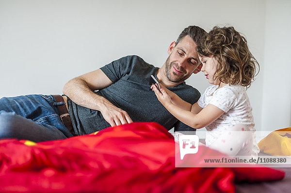 Vater und Tochter mit Handy im Bett