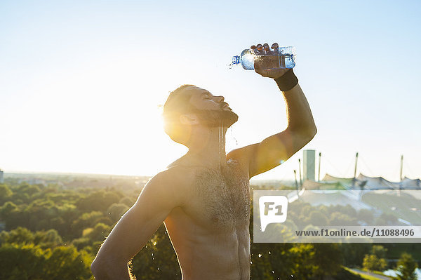 Barechested athlete pouring water over his face at sunset