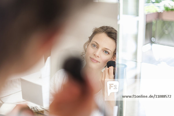 Woman looking in mirror applying eye makeup