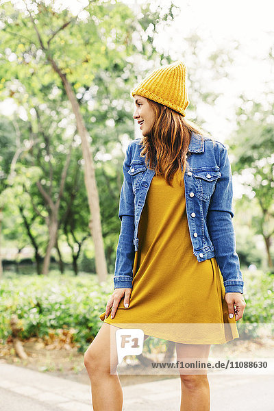 Lächelnde junge Frau mit gelber Mütze und Kleid im Herbst