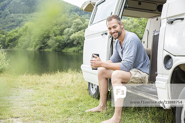 Lächelnder Mann sitzt in einem Van am Seeufer