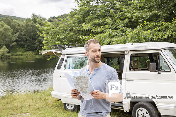 Mann mit Karte an einem Van am Seeufer
