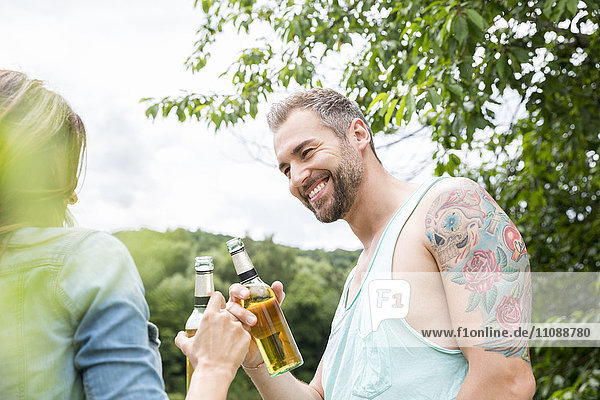 Lächelndes Paar klirrende Bierflaschen in der Natur