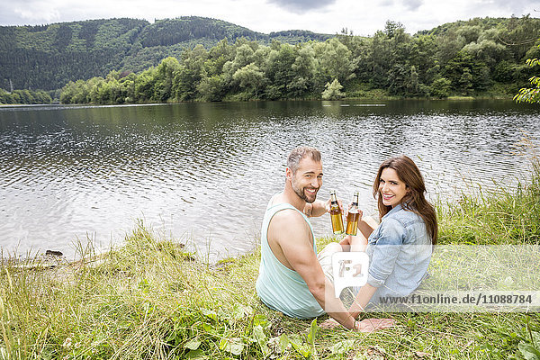 Lächelndes Paar mit Bierflaschen am Seeufer
