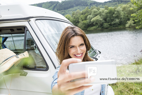 Smiling woman beside van at lakeside taking a selfie