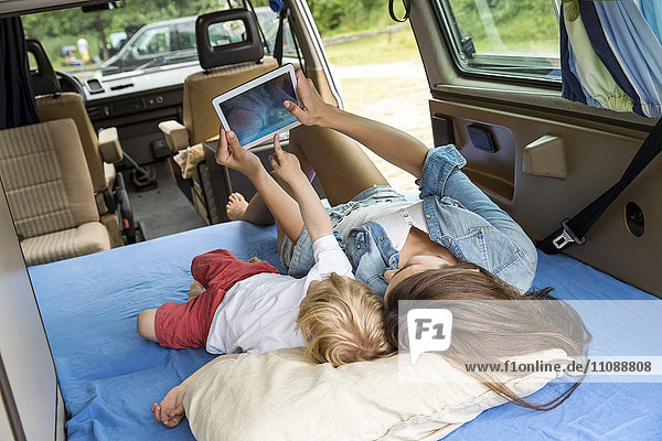 Mutter und Sohn liegen auf Matratze im Van mit Tablette