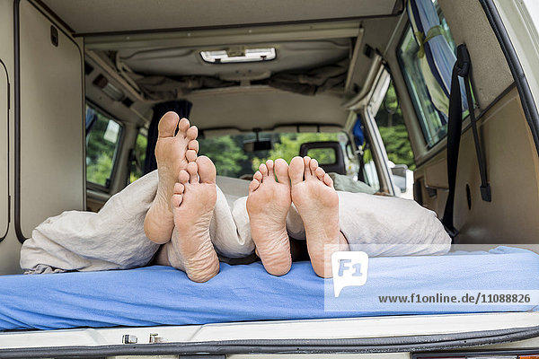 Füße eines Paares auf Matratze im Van liegend