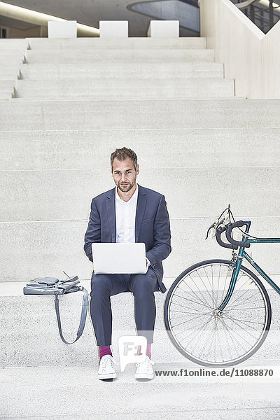 Businesssman on stairs using laptop next to bicycle