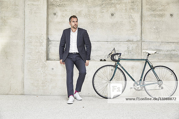Businesssman with bicycle at concrete wall