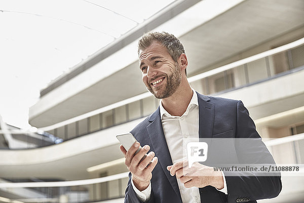 Lächelnder Geschäftsmann im Bürogebäude mit Handy