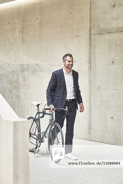 Businesssman pushing bicycle along concrete wall