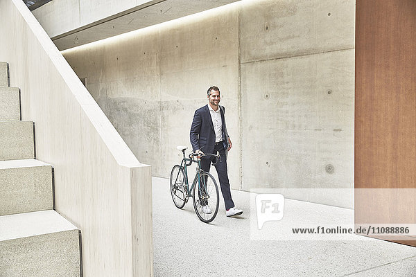 Businesssman pushing bicycle along concrete wall