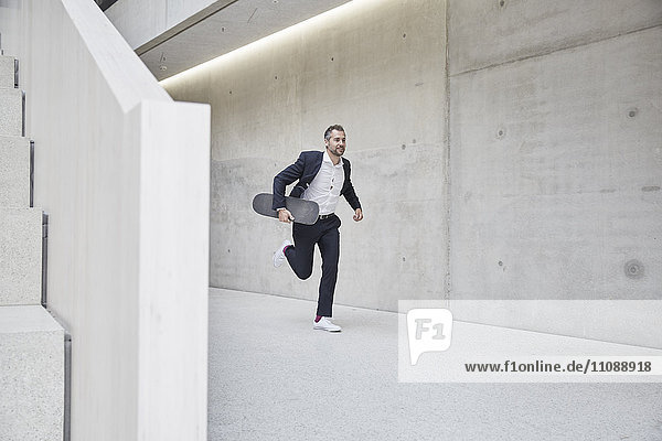 Businesssman running with skateboard along concrete wall