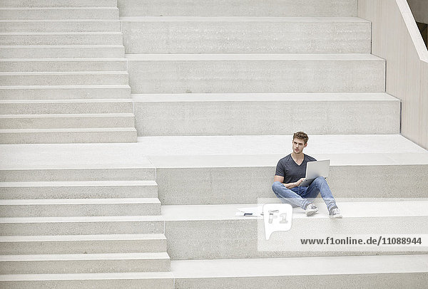 Junger Mann auf der Treppe sitzend mit Laptop
