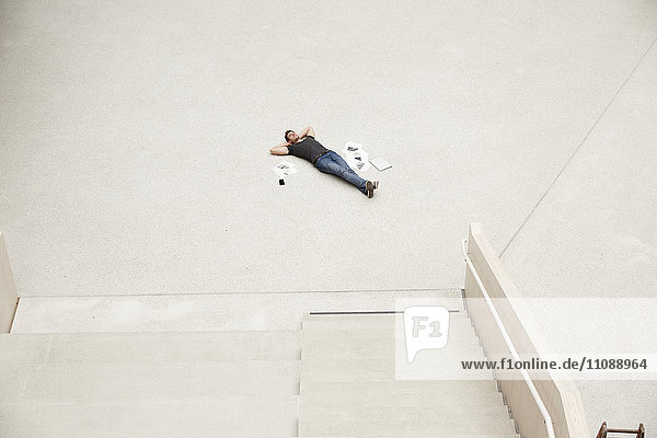 Junger Mann auf dem Boden liegend  umgeben von Papieren.