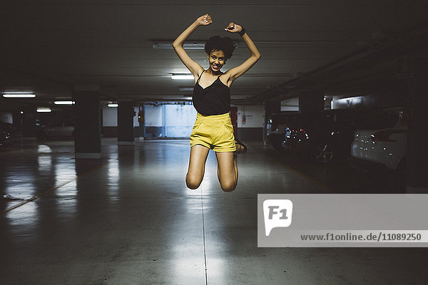 Lächelnde junge Frau  die auf einem Parkplatz in die Luft springt.