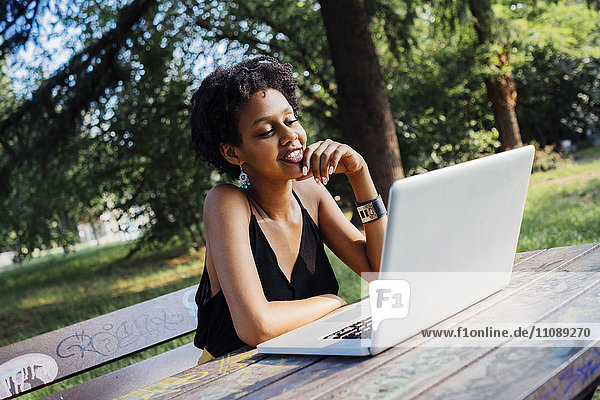 Junge Frau sitzt auf der Parkbank mit Laptop
