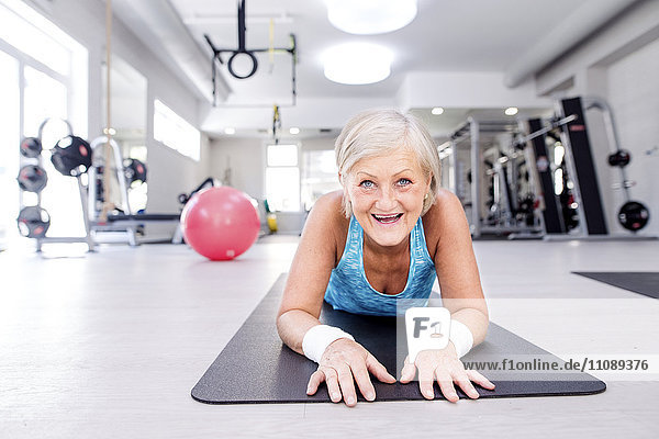 Lächelnde reife Frau  die auf einer Turnmatte im Fitnessstudio liegt.