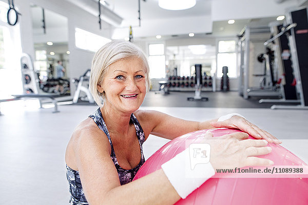 Porträt einer lächelnden reifen Frau mit Fitnessball in der Turnhalle