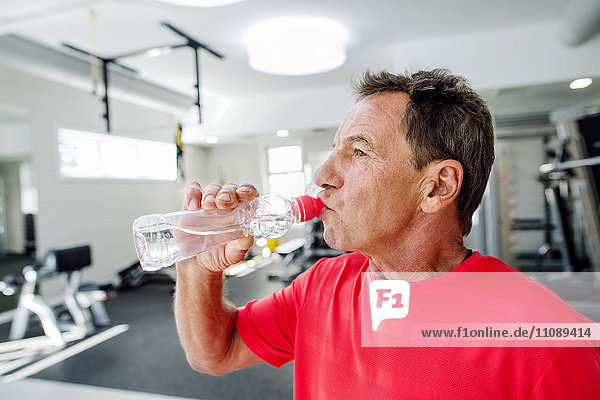 Senior Mann im Fitnessstudio Trinkwasser aus der Flasche