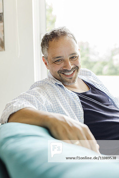 Porträt eines lächelnden Mannes  der zu Hause auf der Couch sitzt.