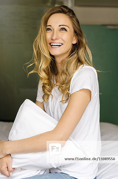 Laughing blond woman sitting on bed holding cushion