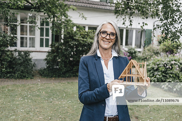 Lächelnde Geschäftsfrau mit Architekturmodell im Garten