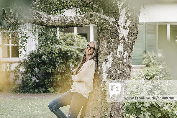 Lächelnde Frau  die sich im Garten an den Baum lehnt